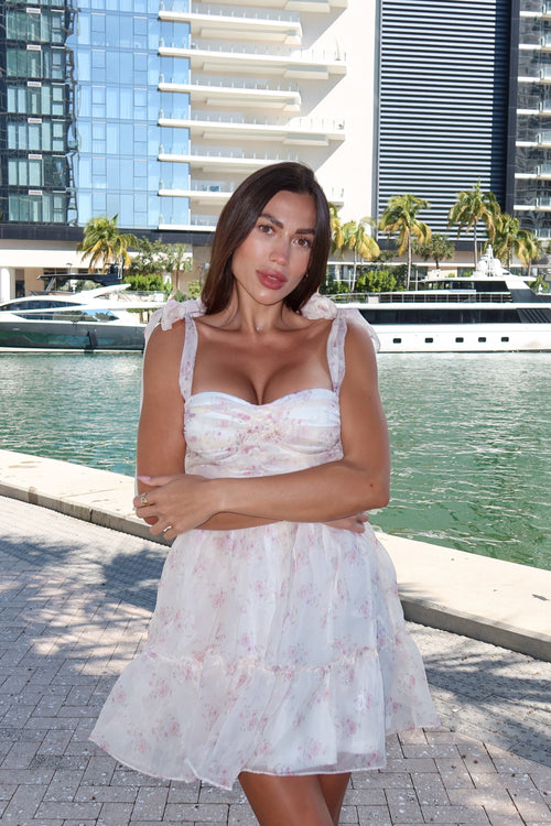 Woman in a white dress standing by a waterfront with buildings and boats in the background