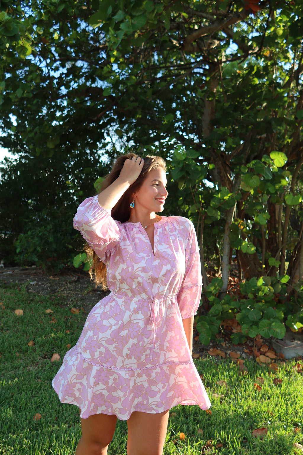 Woman in a pink floral dress standing outdoors with greenery in the background